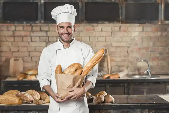 male baker holding loaf of breads in paper bag