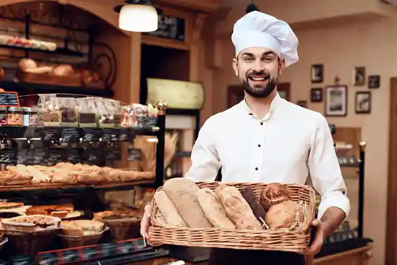 Young man in white cap standing in bakery with bakery items.